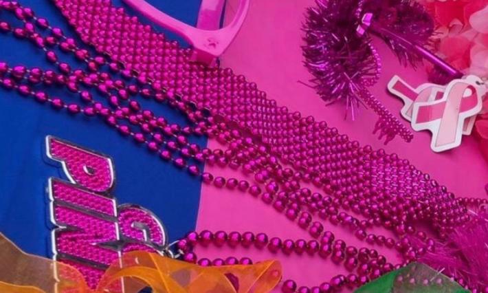 A collection of pink and colorful items (necklaces, glasses, boas) are arranged on a table