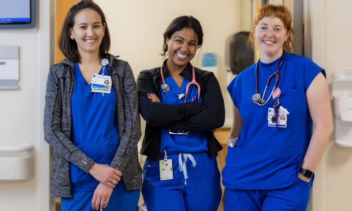 Three Duke Health nursing team members pose together smiling in the doorway of a patient room.