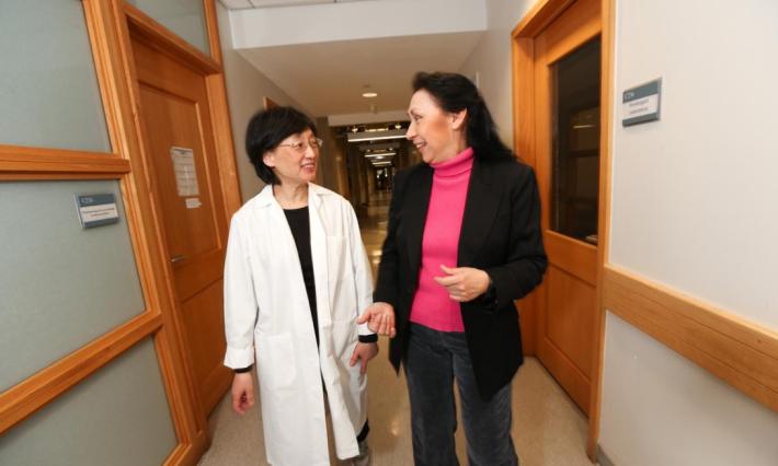 two women, one in a labcoat, walk and talk in a hallway