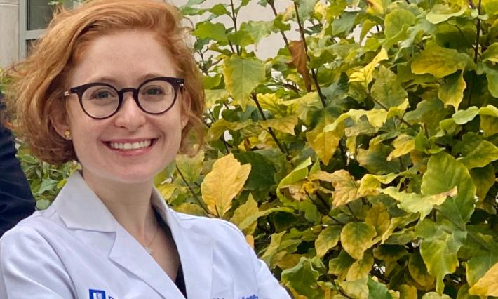 woman stands in front of bush of yellow leaves in a lab coat that reads "Duke Health, Haley Moss, MD"
