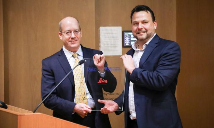 Lawrence Carin, PhD, and Greg Eppink pose with a special glass plaque created for the new Leica Microsystems Center for Excellence 