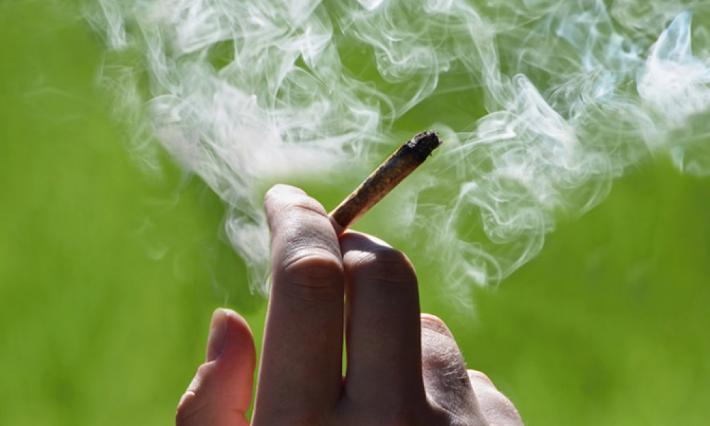fingers holding a marijuana cigarette with smoke around it