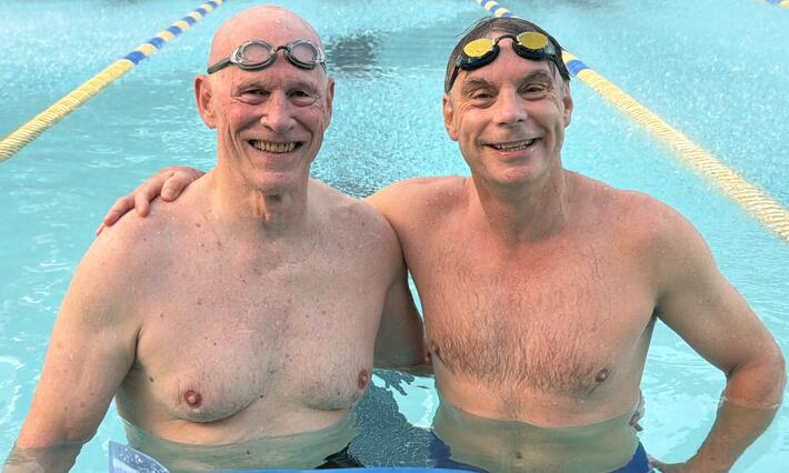 Two men wearing bathing suits standing at the end of a lap pool