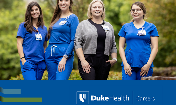 Four nurses smile in scrubs and professional attire outside Duke University Hospital.
