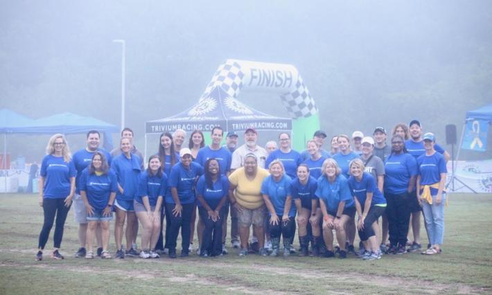 About two dozen Team DCI members clad in blue shirts gather on a misty field