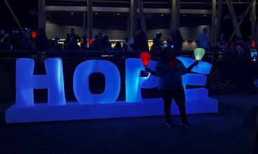 a blue inflated "Hope" sign is illuminated. A woman holds a red and a white lantern.