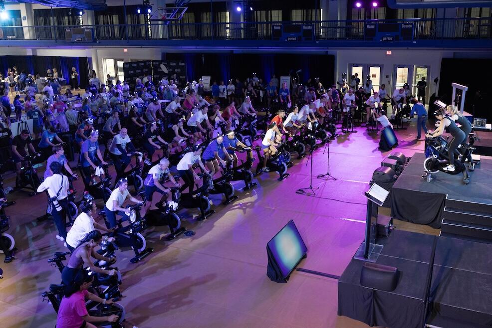 Crowd of people riding stationery bikes indoors with blue lighting