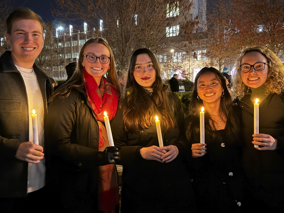 Five young adults stand in front of Duke Cancer Center holding lit candles