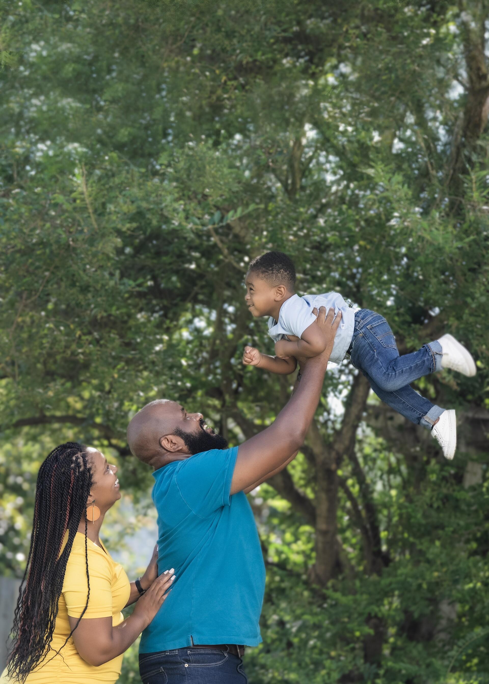 Richard Brown playfully lifting toddler Andrew in the air as mom Arlene Brown looks on, smiling.