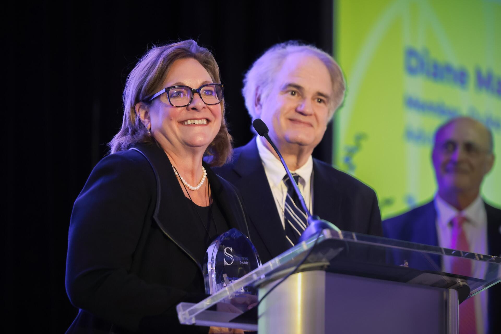 2.	A couple at a lectern smiling together at the Shingleton awards reception.