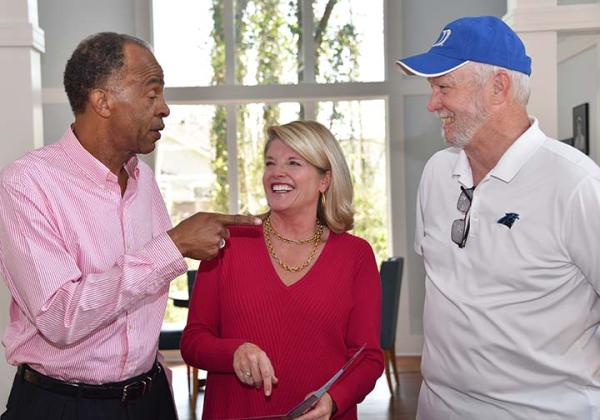 John Sanders, wearing a pink shirt, points at Tom Shankle, who's smiling and wearing a Duke cap while Sheridan van Wagenberg in red, standing between them, smiles at John.