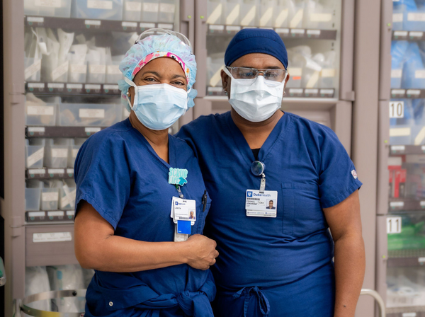 Two Duke Health team members dressed in blue scrubs, surgical masks, and caps stand together in the OR.
