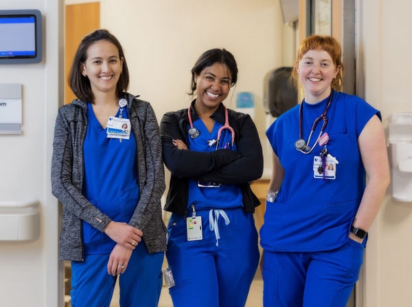 Three Duke Health nursing team members pose together smiling in the doorway of a patient room.