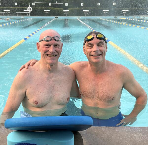 Two men wearing bathing suits standing at the end of a lap pool
