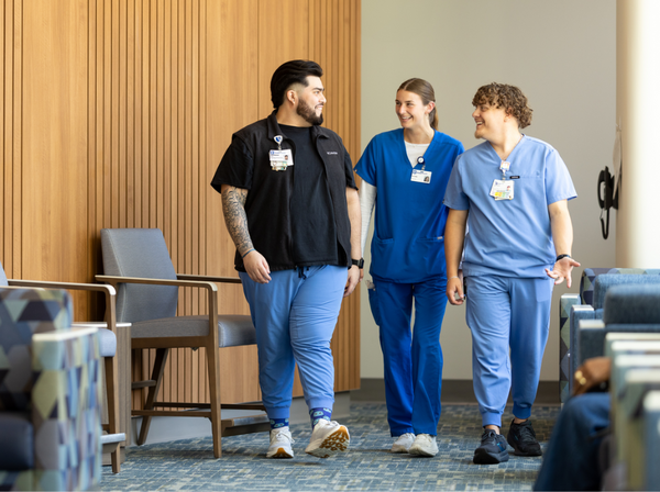 Three Duke Health team members wearing scrubs of varying shades of blue walk together through the hospital hallway.