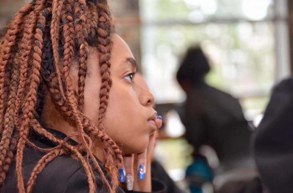 A student with braids in her hair listens intently with one hand under her chin. 