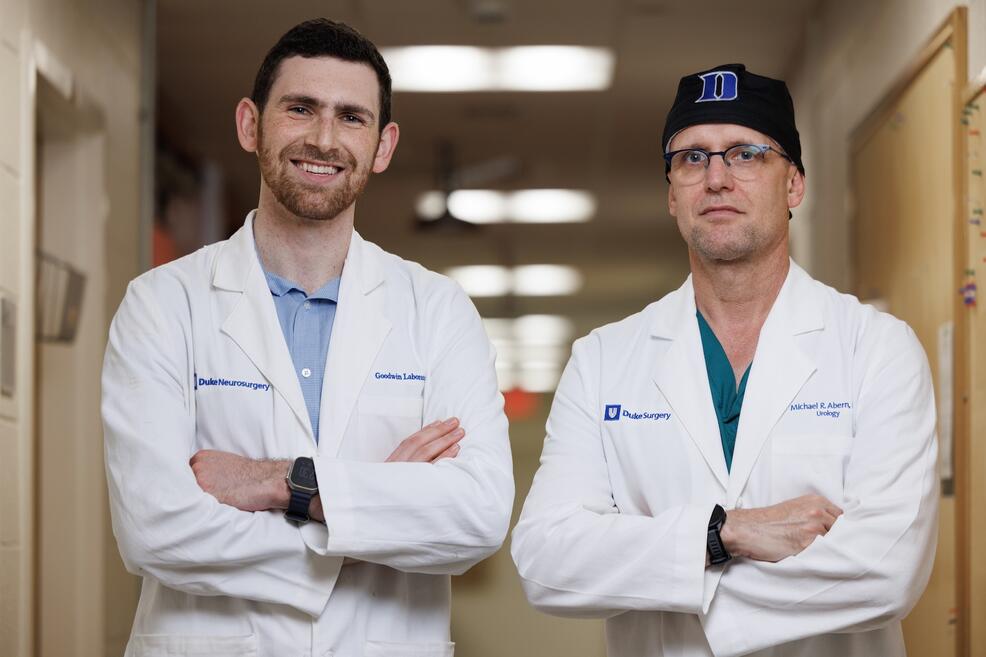 Two men in white coats standing side by side, looking at the camera intently.