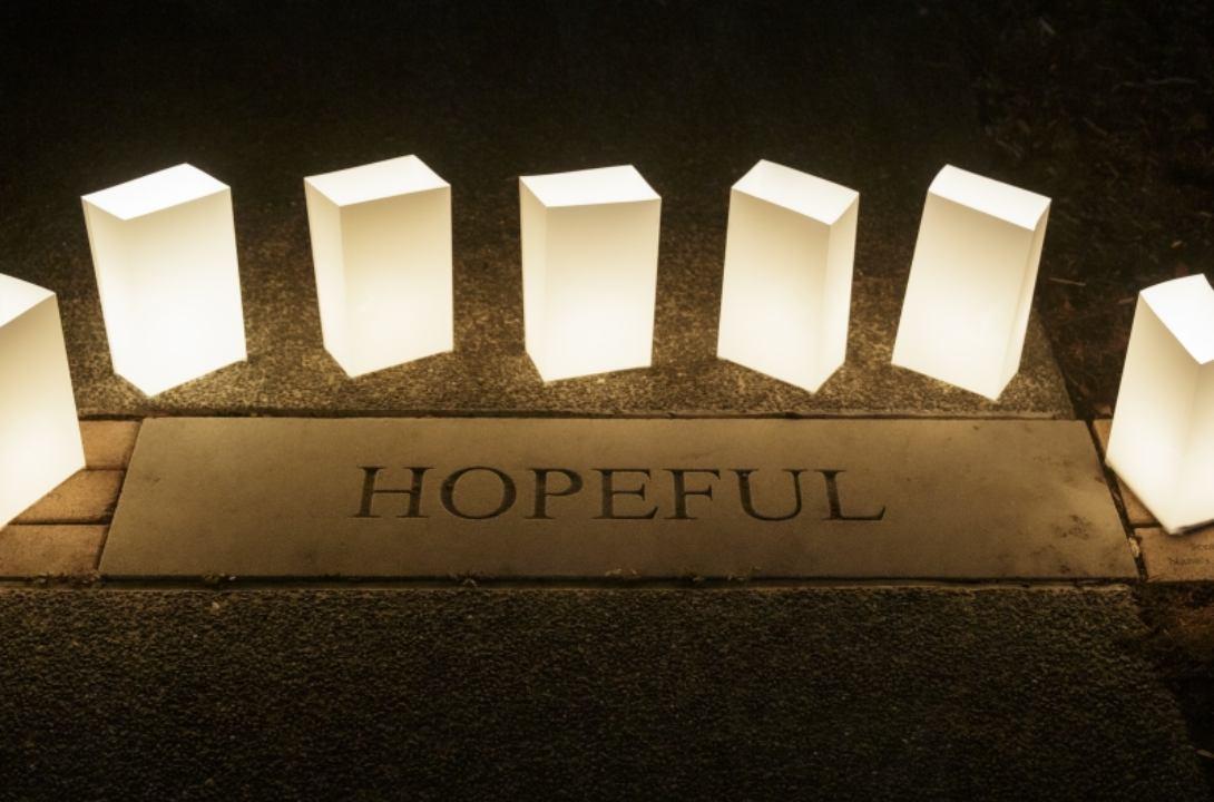 A semicircle of white luminaries light up the word "Hopeful" that is stamped in concrete.