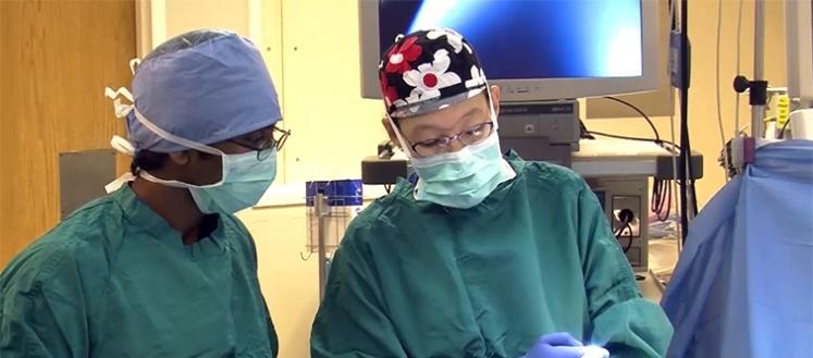 Betty Tong looks downward in an operating room. Another person stands beside her.