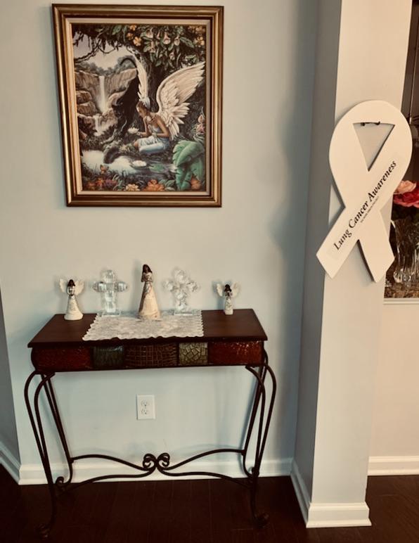 A piece of artwork hangs above a small wooden side table. On the wall beside it hangs a large white cardboard ribbon.