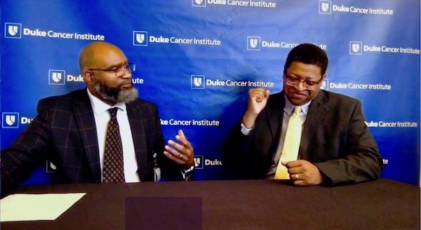Tristan Evans and Angelo Moore talk in front of a "Duke Cancer Institute" background