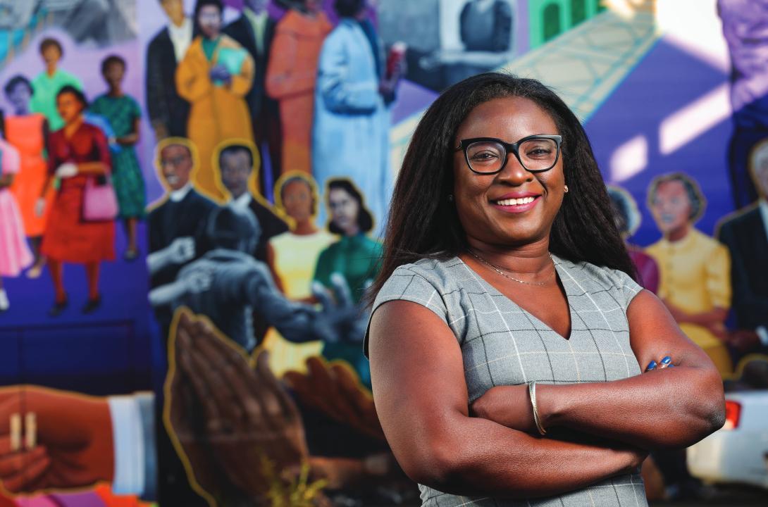 Tomi Akinyemiju smiles with arms folded in front of a colorful mural