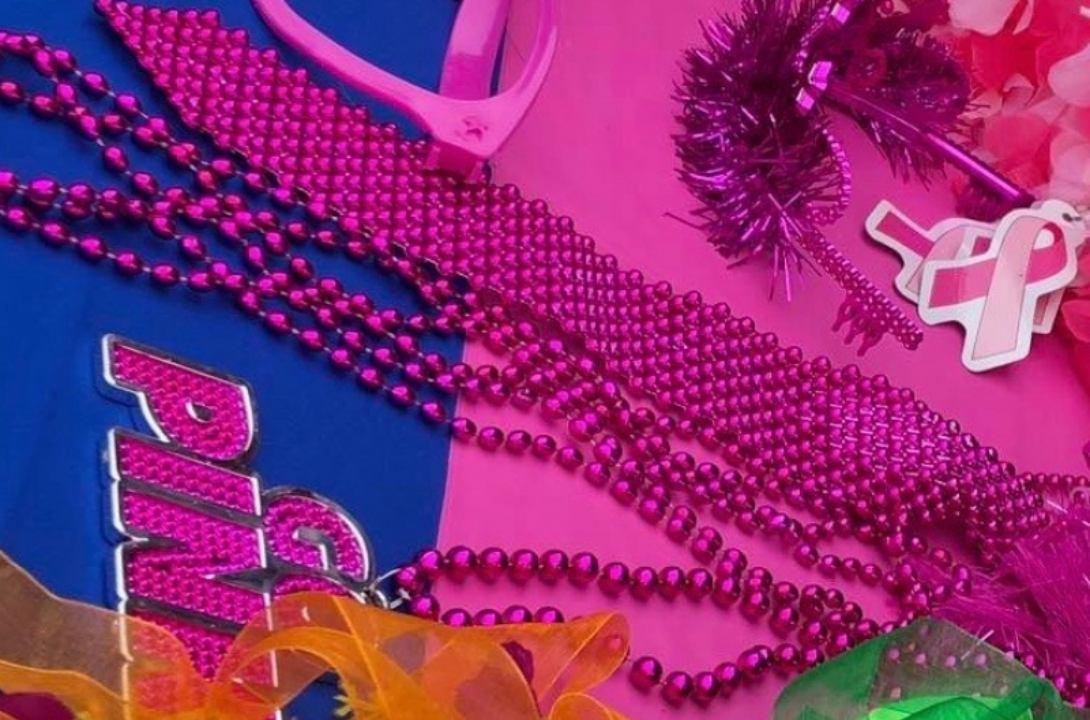 A collection of pink and colorful items (necklaces, glasses, boas) are arranged on a table