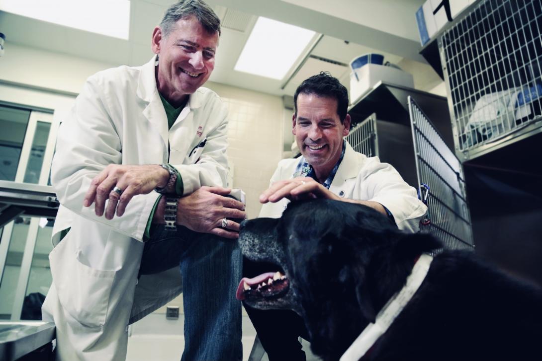 Two men in white coats with black dog