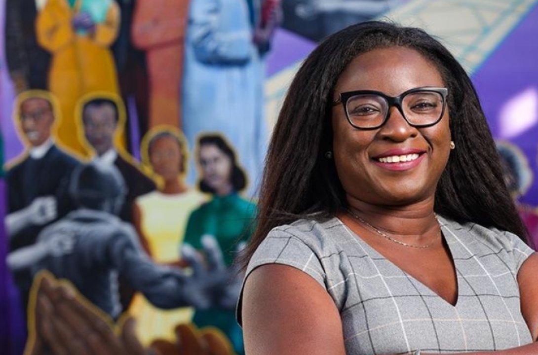 Tomi Akinyemiju, PhD smiles in front of a mural