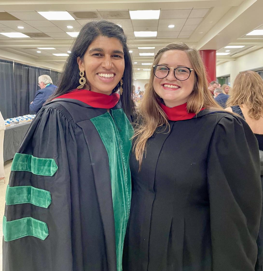 Two women stand together in their black graduation gowns