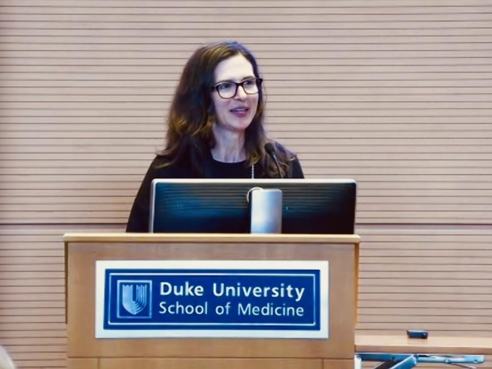 woman speaking at podium labeled Duke University School of Medicine