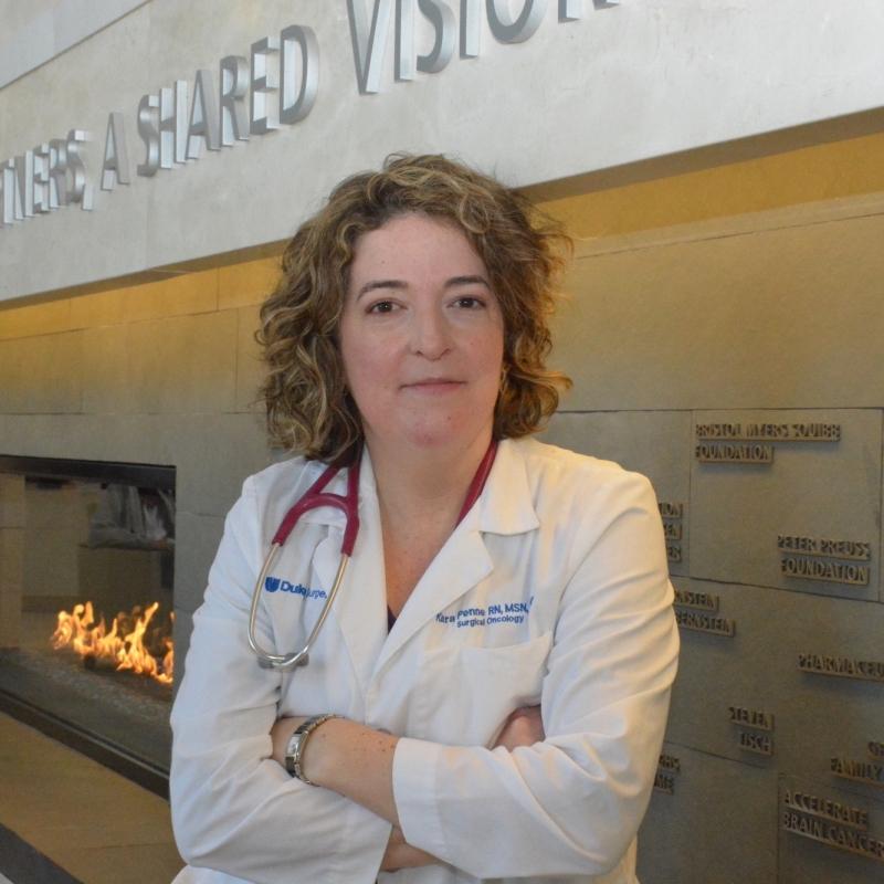 Woman in a white lab coat with a stethoscope in front of a yellow brick wall with the words shared vision, next to a fireplace