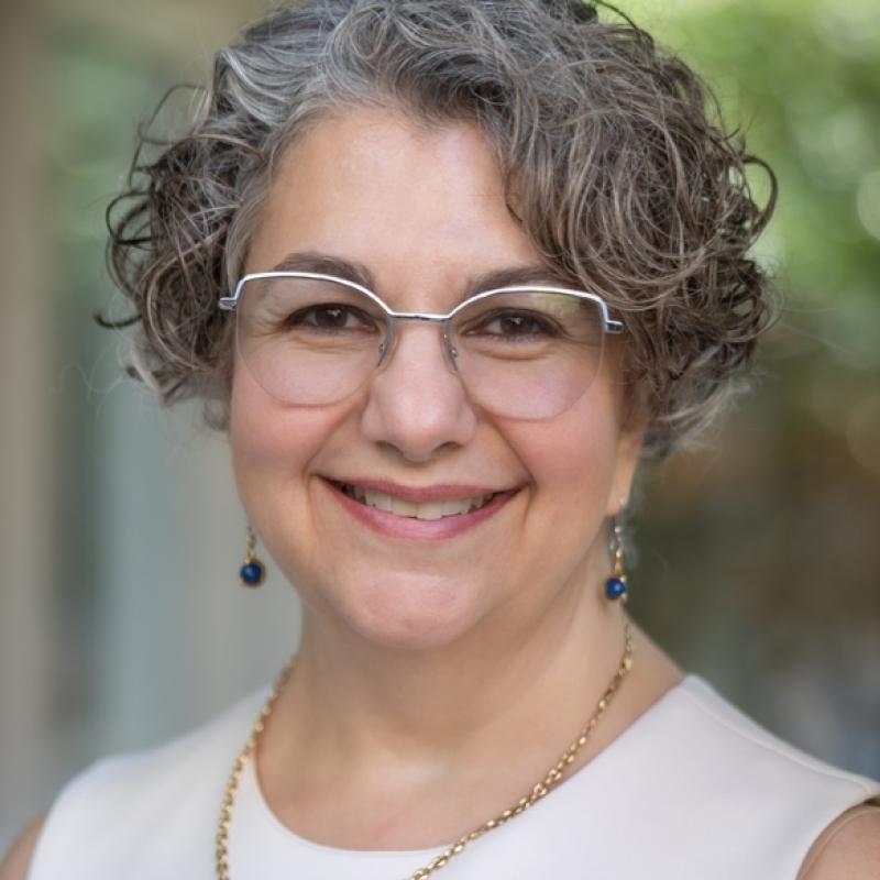 headshot of woman with grey curly hair and glasses, smiling