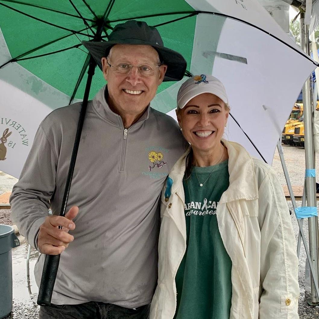 Man and woman in hats, coats, smiling under a big green and white umbrella