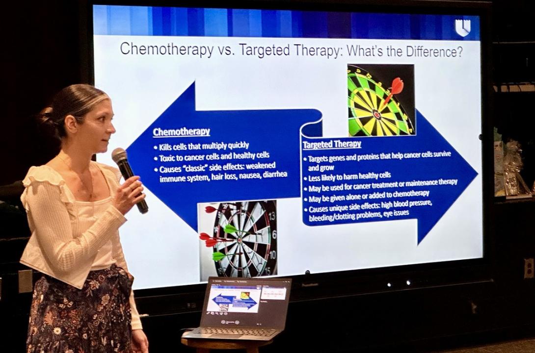 Woman with microphone stands to the side of a projected slide that outlines the differences between chemotherapy and targeted therapy treatments
